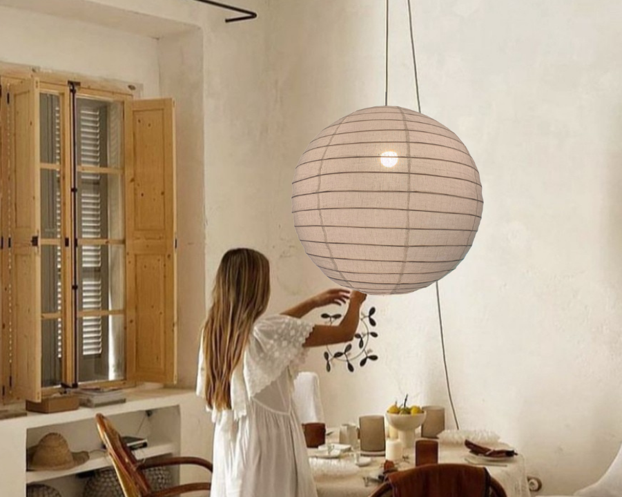 Woman adjusting a pendant light in a cozy room with wooden furniture and neutral decor.