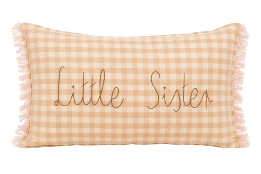 A rectangular throw pillow with a peach and white gingham check pattern, featuring the words 'Little Sister' embroidered in brown cursive across the center and fringed edges.