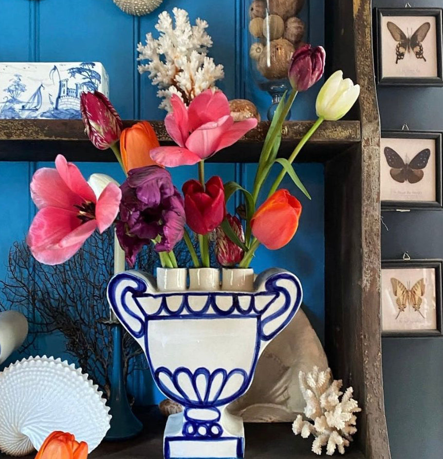 Decorative display with flowers in a blue and white vase against a blue wall.