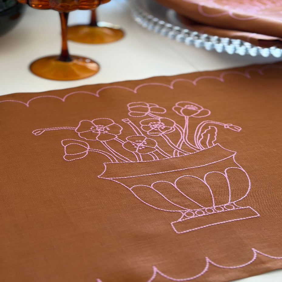 tan linen fabric with pink floral embroidery scalloped border on a white surface side angle