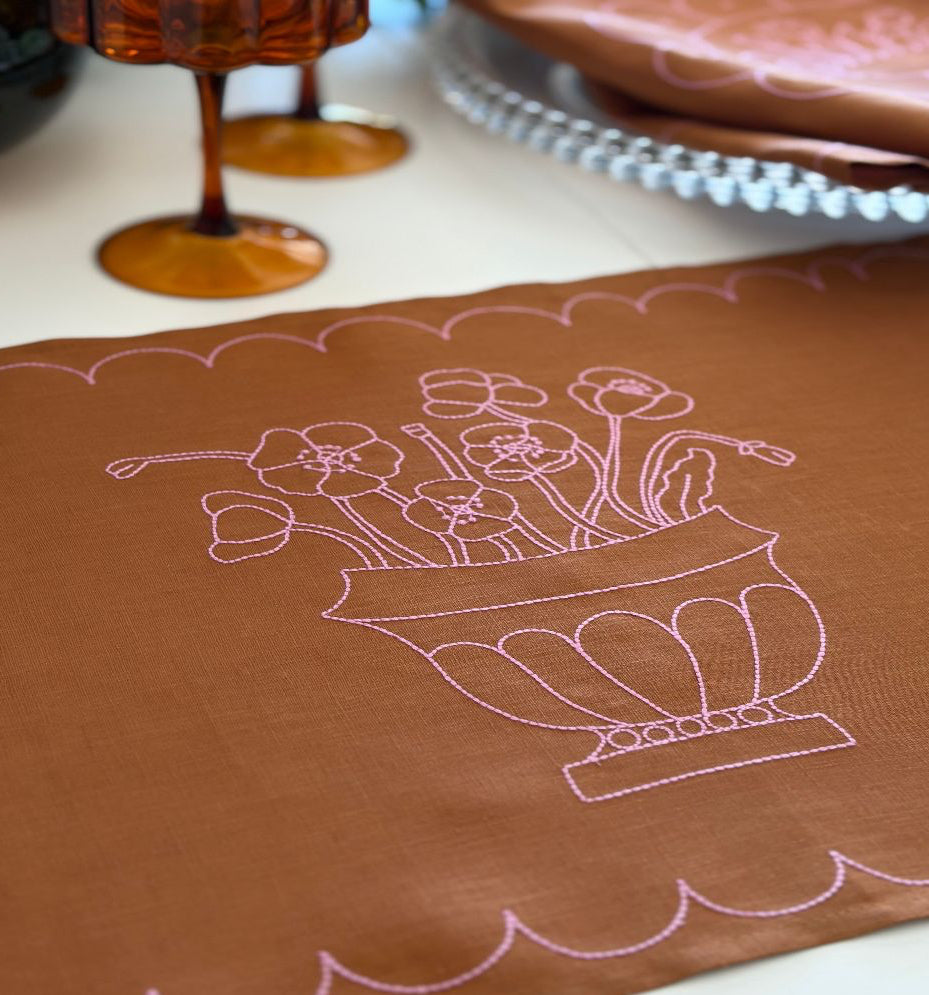 tan linen fabric with pink floral embroidery scalloped border on a white surface side angle
