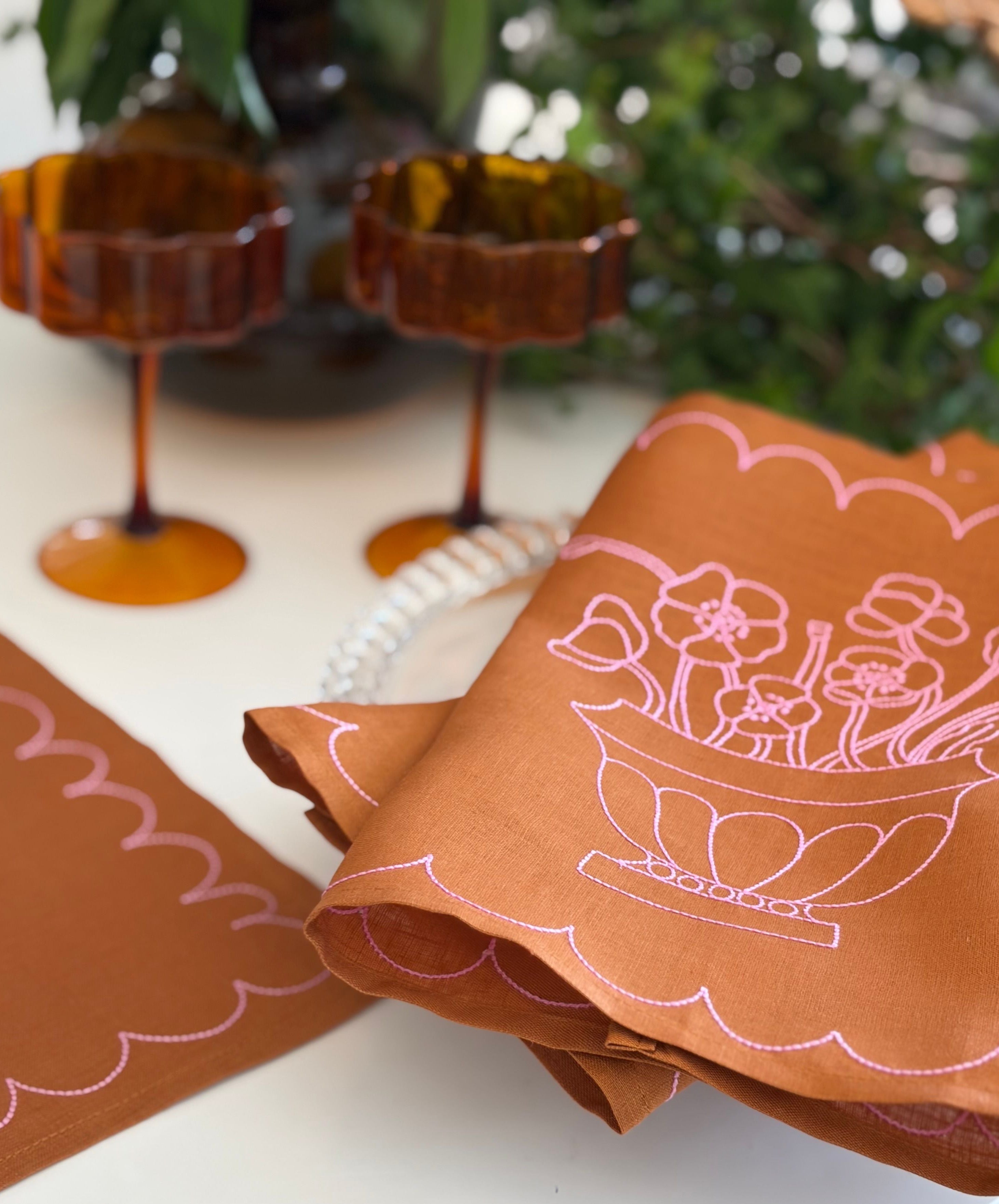 Tan linen fabric placemat with pink embroidery on a table with decorative items in the background
