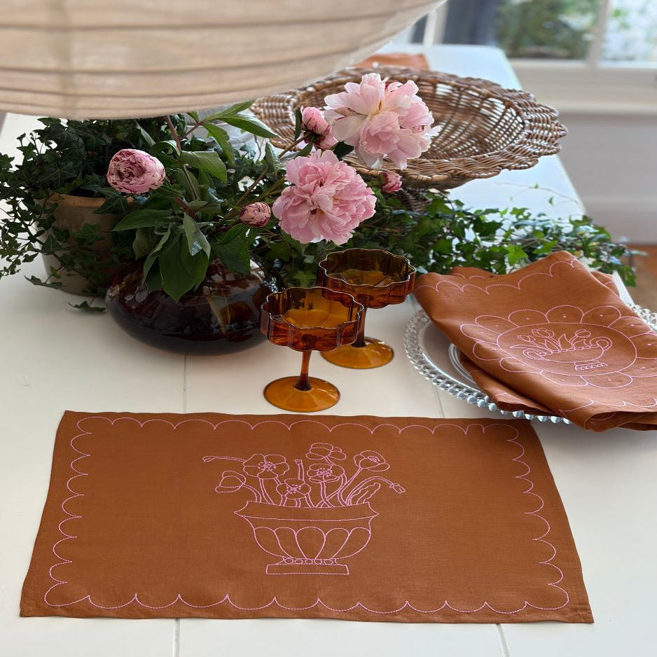 Decorative tan linen with pink embroidery placemat with floral design on a table with flowers and glasses Jane paquin - bowden x littlenordic sol collaboration 