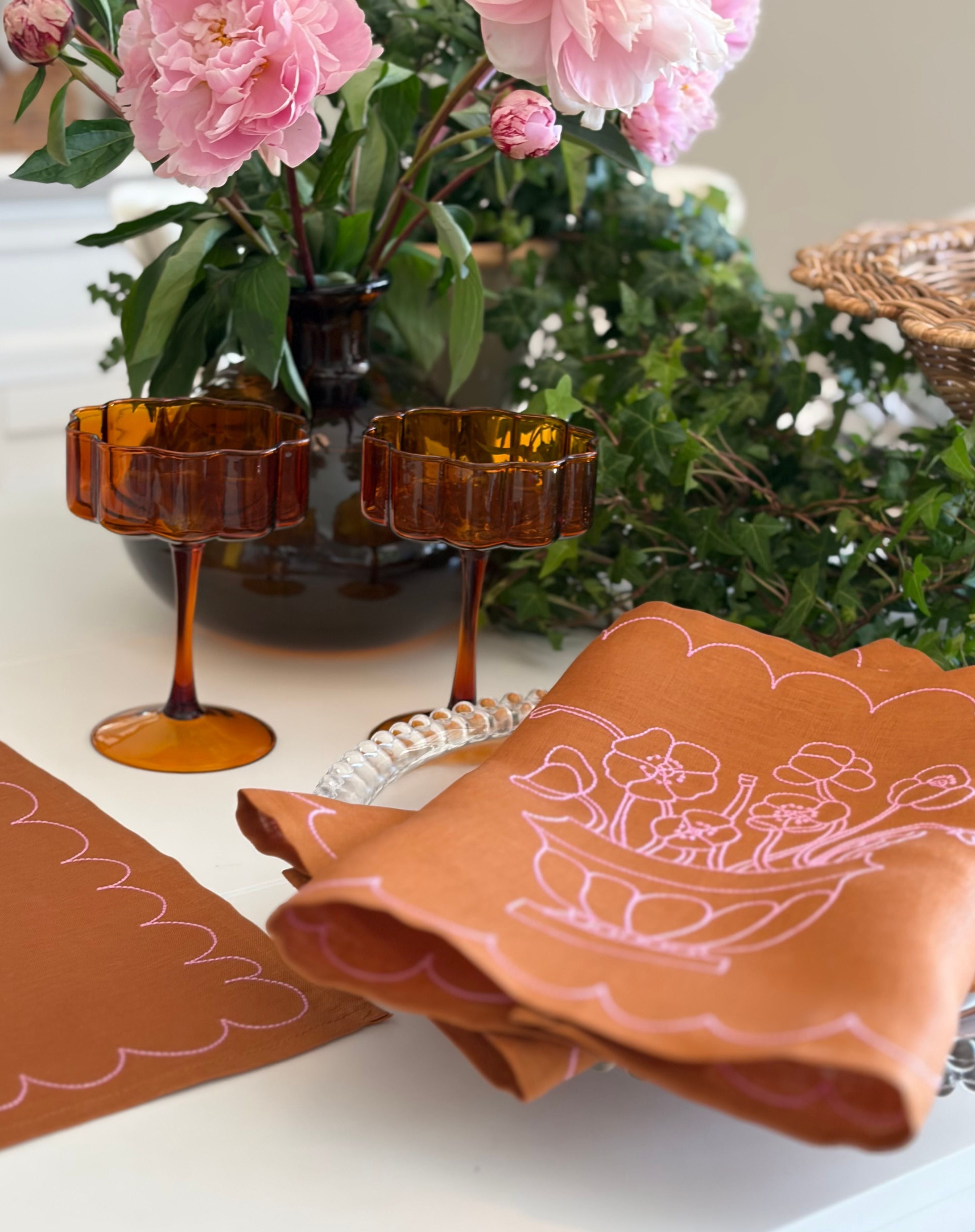 Decorative table setting with brown napkins, amber glassware, and floral arrangements.