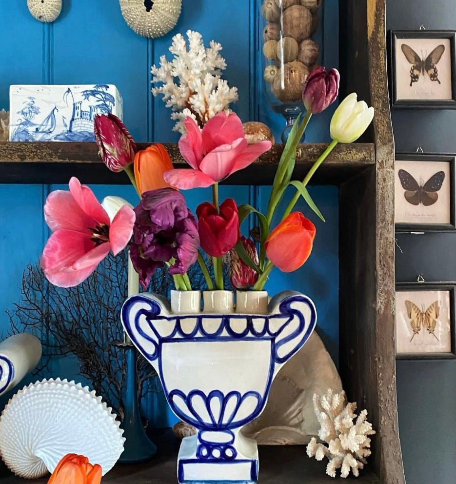 Decorative display with colorful flowers in a blue and white vase against a blue wall.