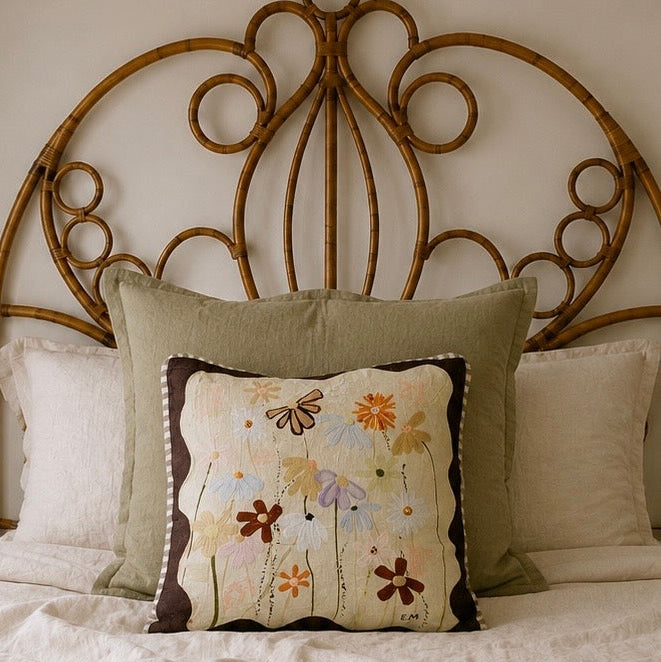 Little Nordic Sol Lost in You Sisterhood floral cushion styled with olive and neutral cushions against a rattan bedhead