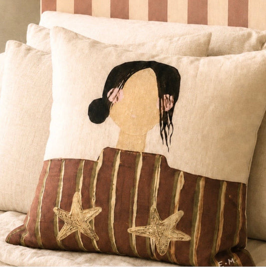 Little Nordic Sol Olive illustrated linen cushion with striped girl and gold stars styled on neutral bedding