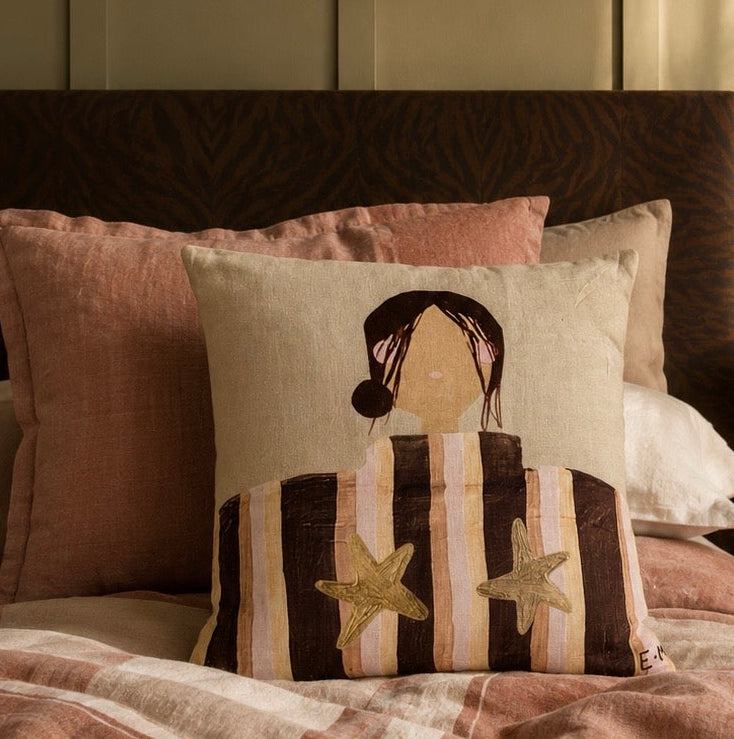Little Nordic Sol Sadie illustrated linen cushion with striped girl and gold stars styled on blush bedding