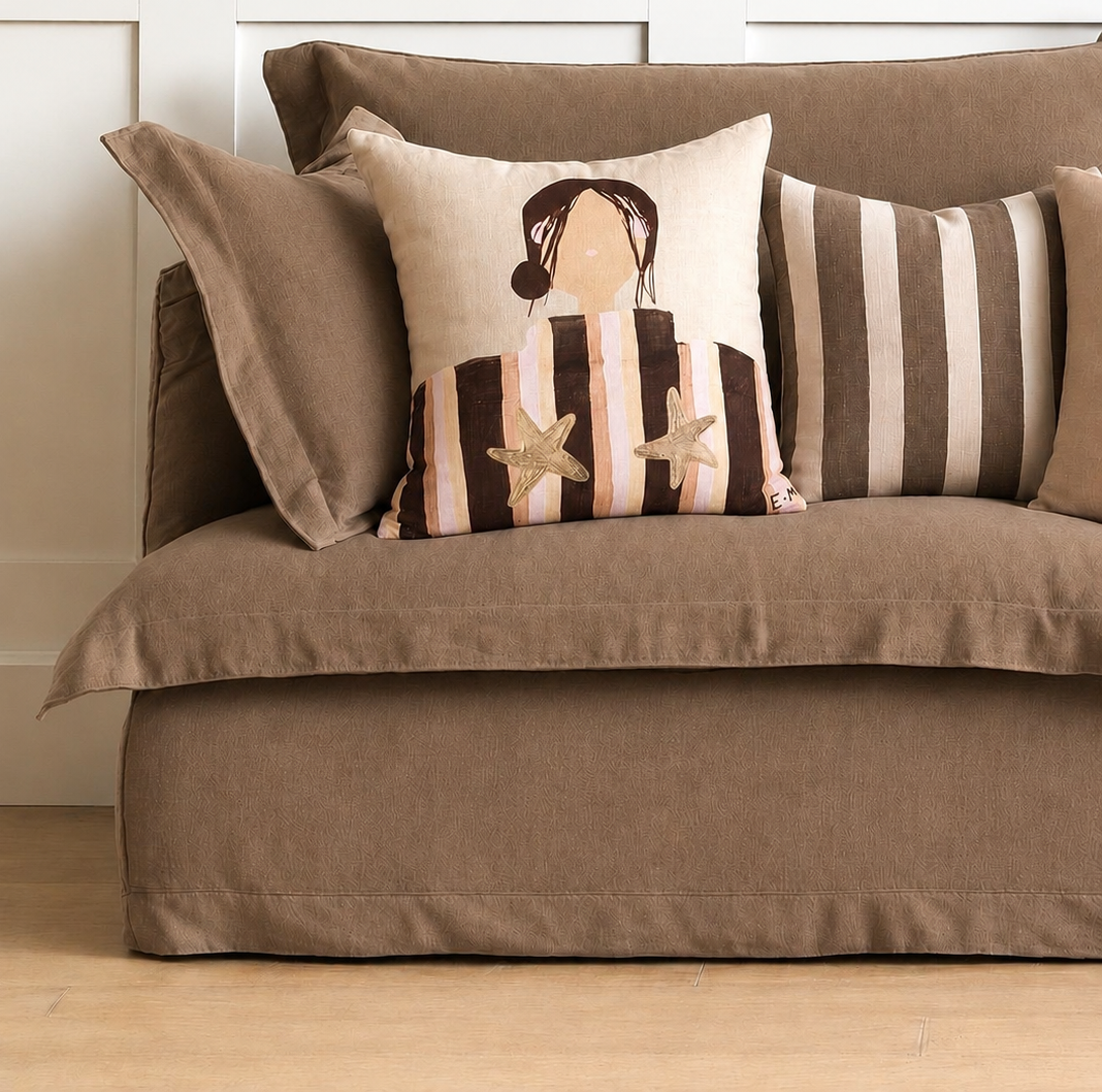 Little Nordic Sol Sadie illustrated linen cushion styled with a striped cushion on a taupe sofa