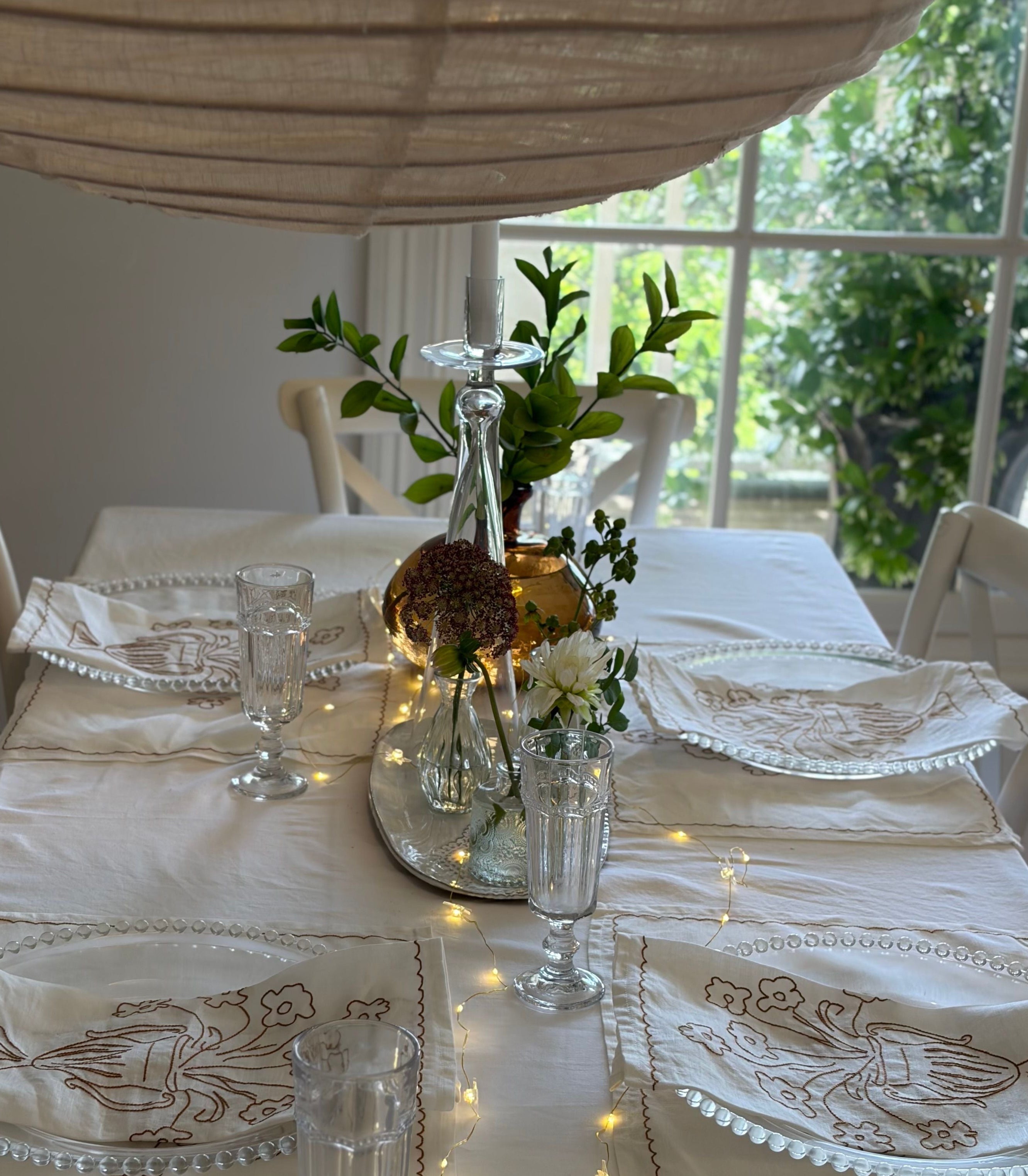 Elegant table setting with white tablecloth, decorative plates, and centerpieces in a bright room.