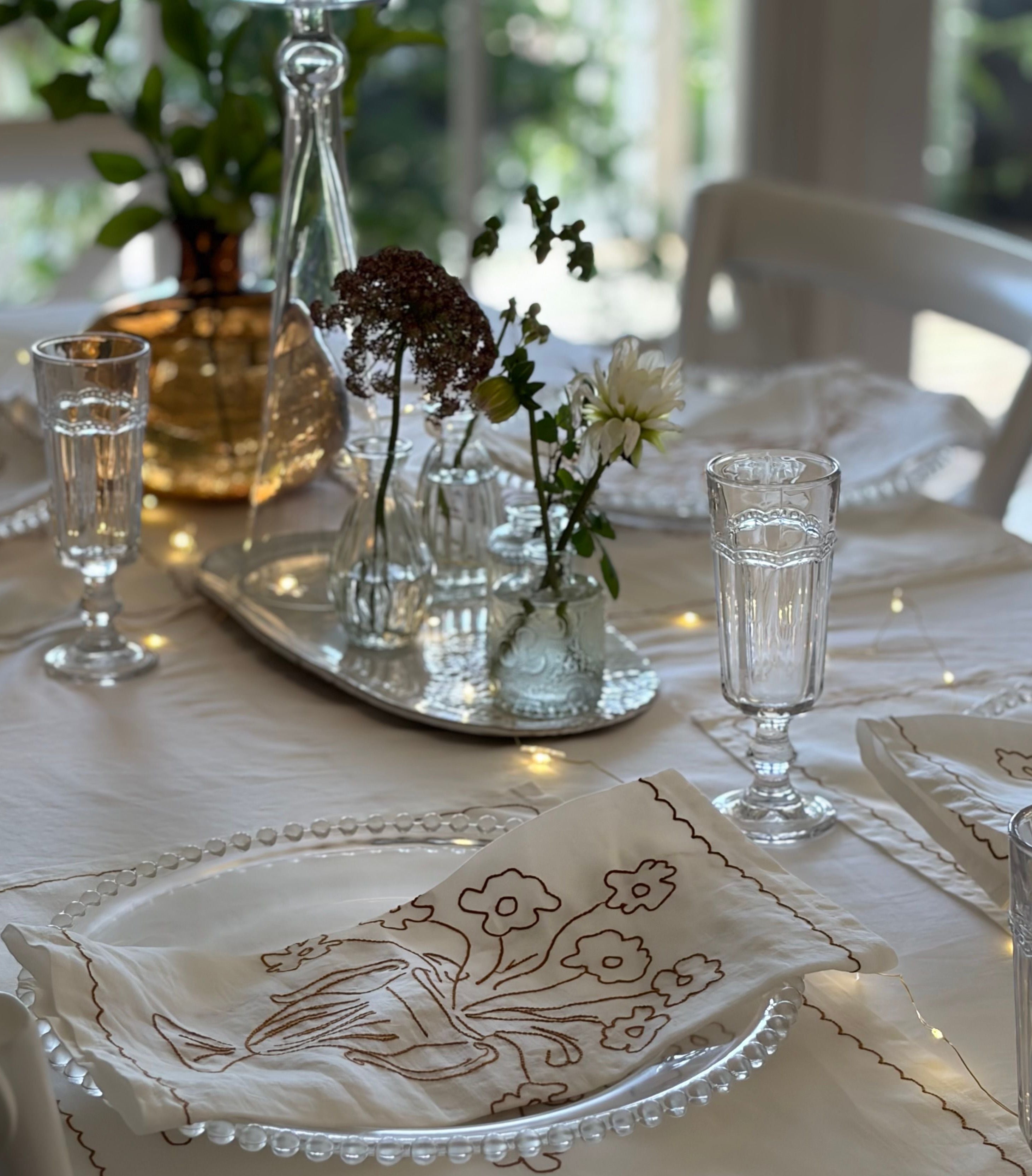 Dining table setting with floral arrangement, glasses, and embroidered napkins.