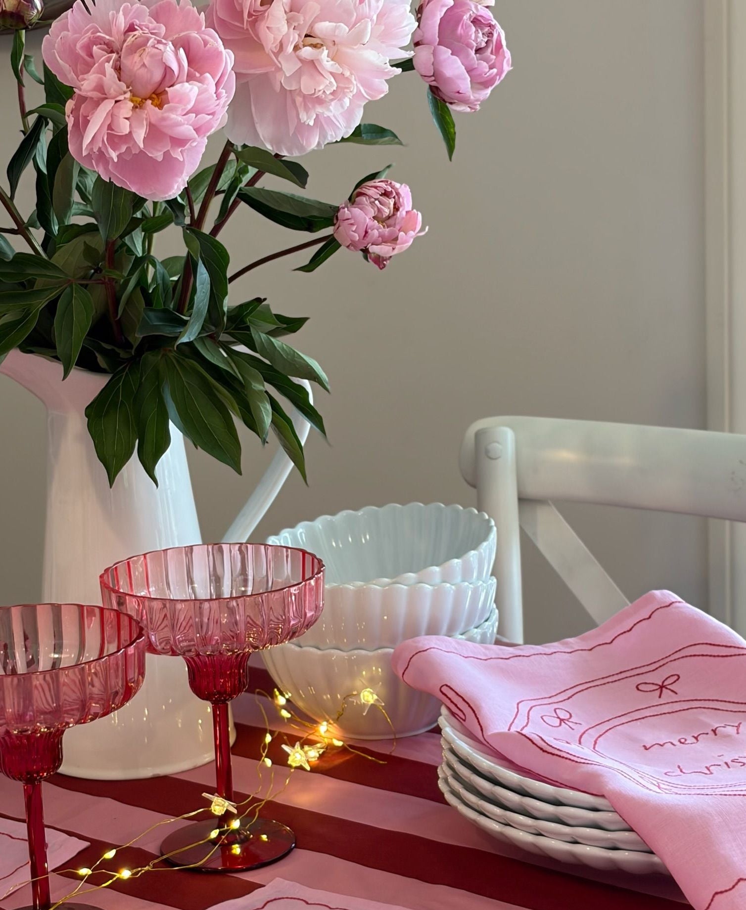 Pink floral arrangement in a white vase on a table with pink and red glassware, white bowls, and a pink cloth.