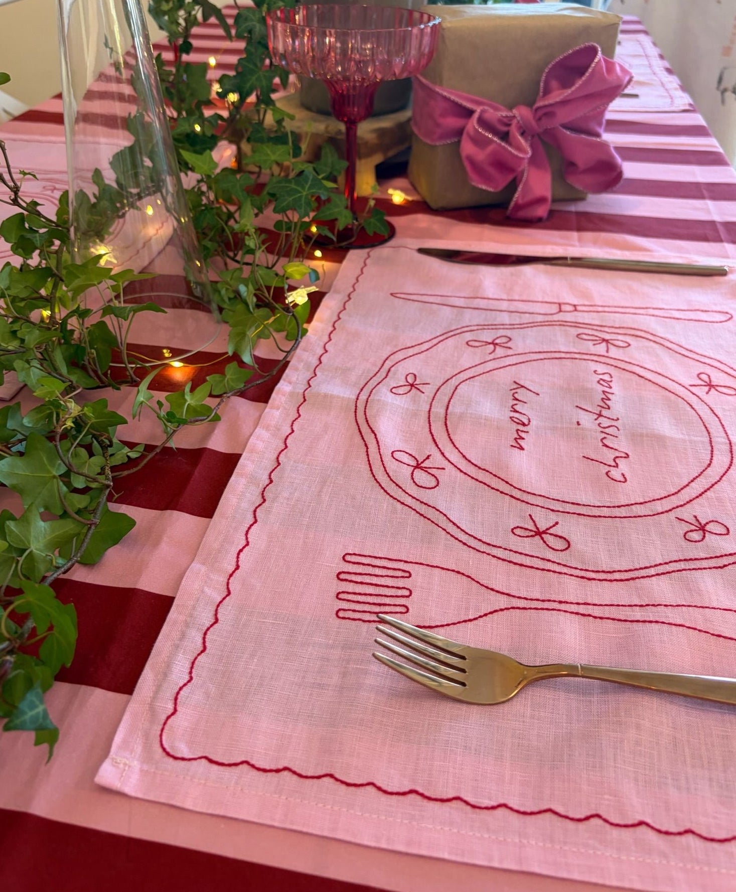 Pink Christmas-themed placemat on a table with a red and white checkered tablecloth.