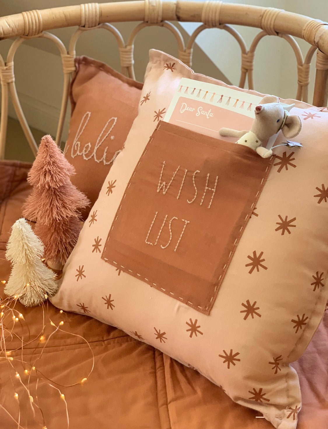 Decorative pillow with 'Wish List' text on a bed with plush toys and fairy lights.