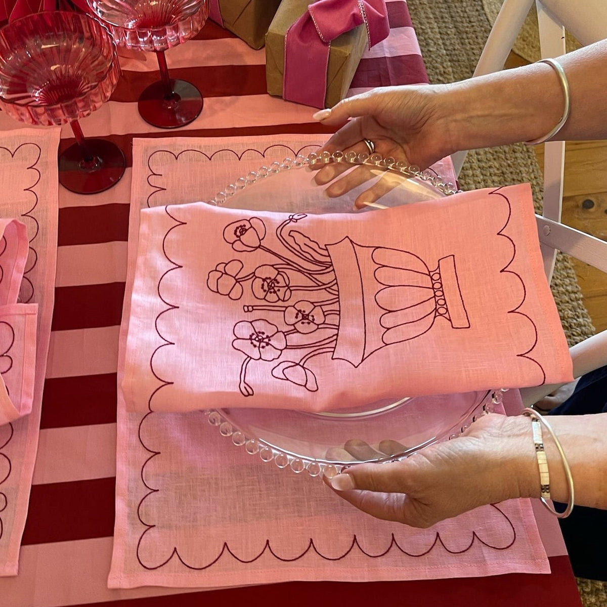 Person holding a pink embroidered napkin with a design on a red and white striped tablecloth.
