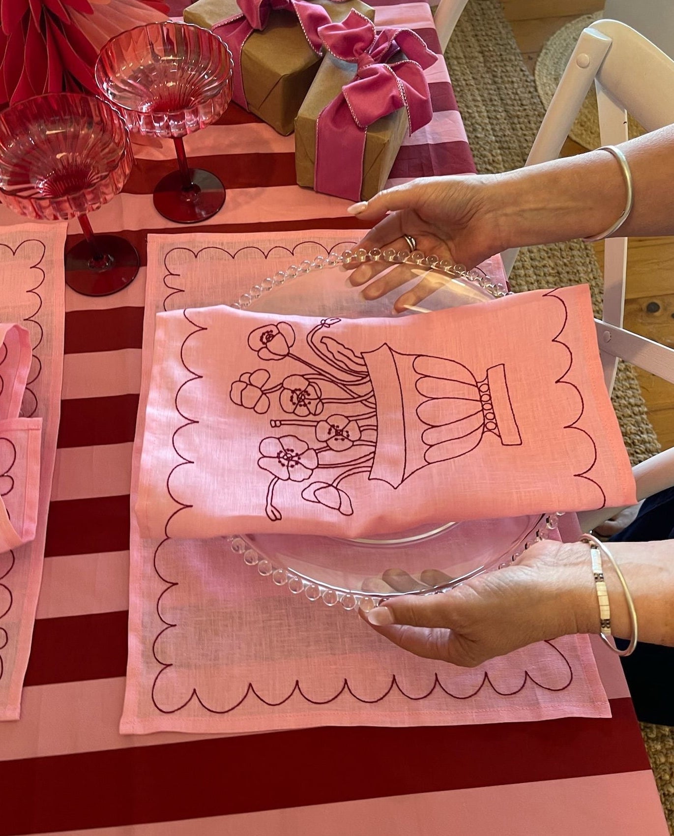 Person holding a pink embroidered napkin with a design on a red and white striped tablecloth.