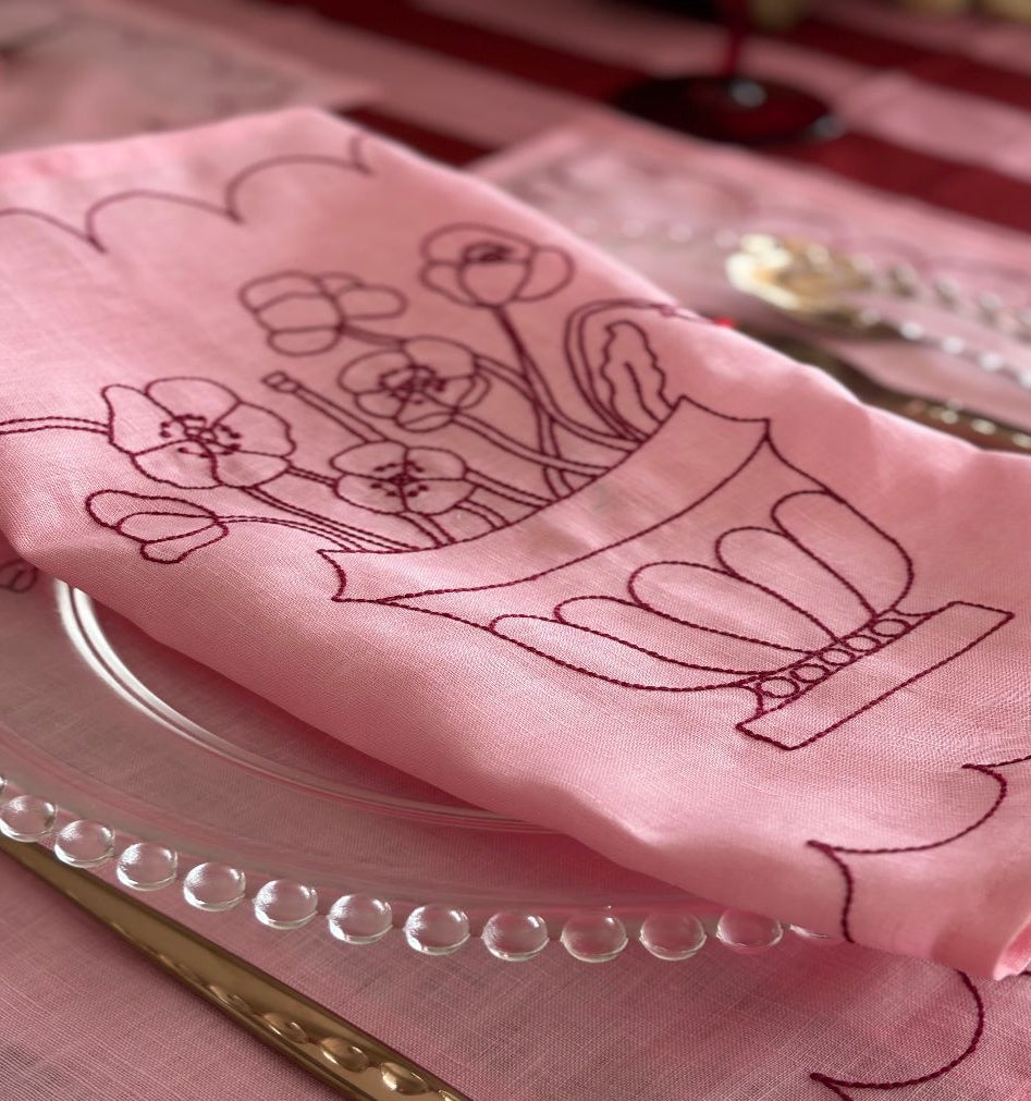 Pink embroidered napkin on a glass plate with silverware in the background