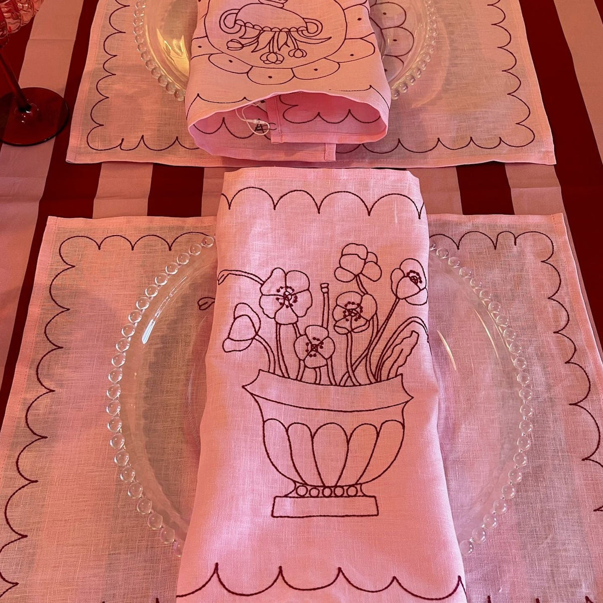 Pink placemats and napkins with floral designs on a red and white checkered tablecloth.