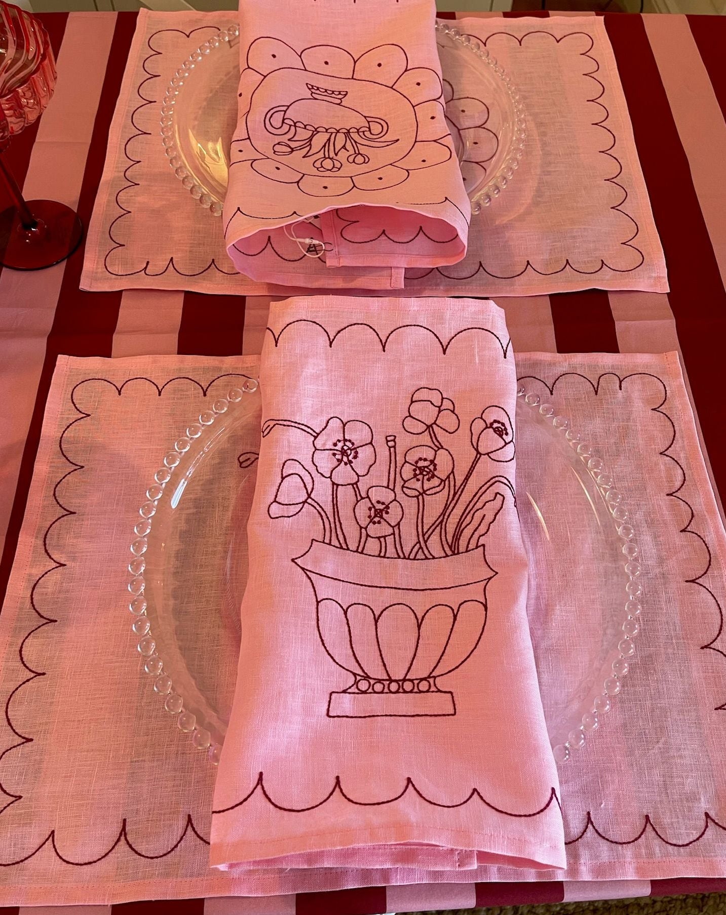Pink placemats and napkins with floral designs on a red and white checkered tablecloth.