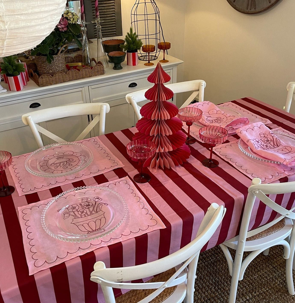 Dining table set with red and white striped tablecloth, pink placemats, and decorative items in a room.