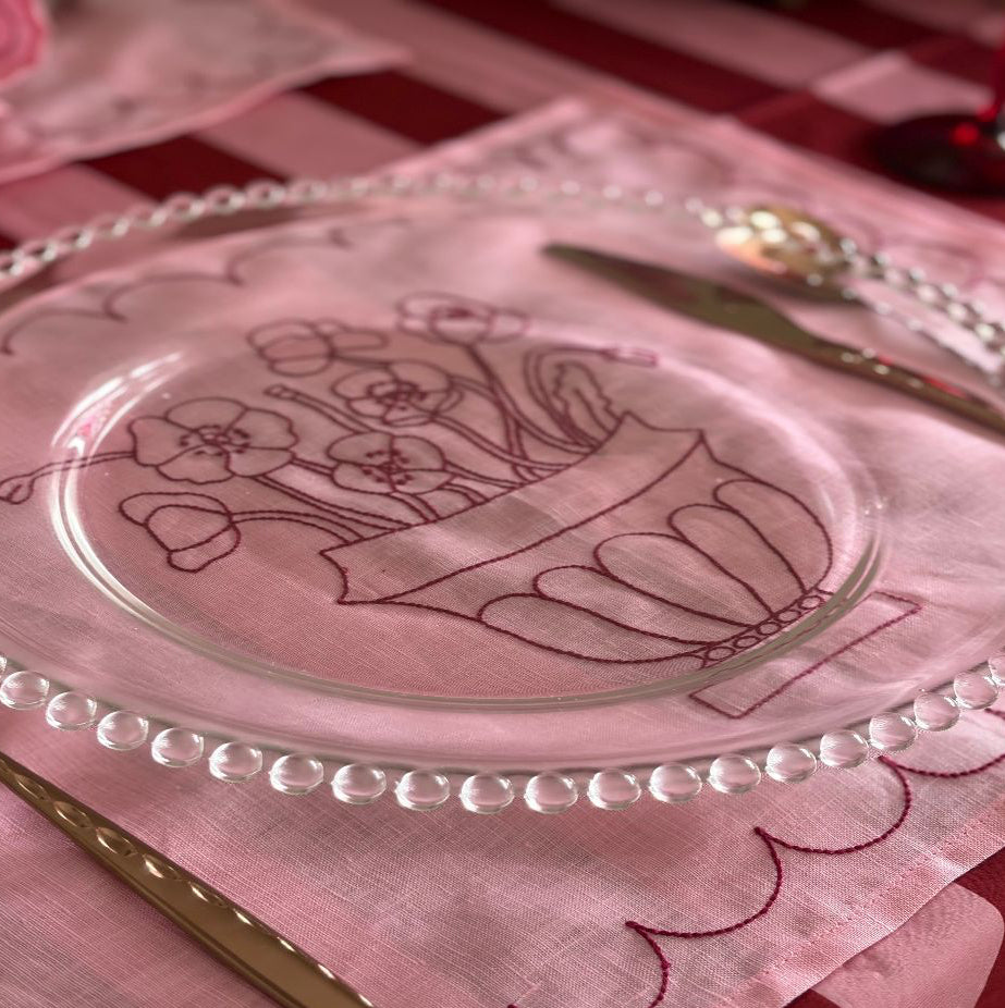 Decorative glass plate with floral design on a pink tablecloth.