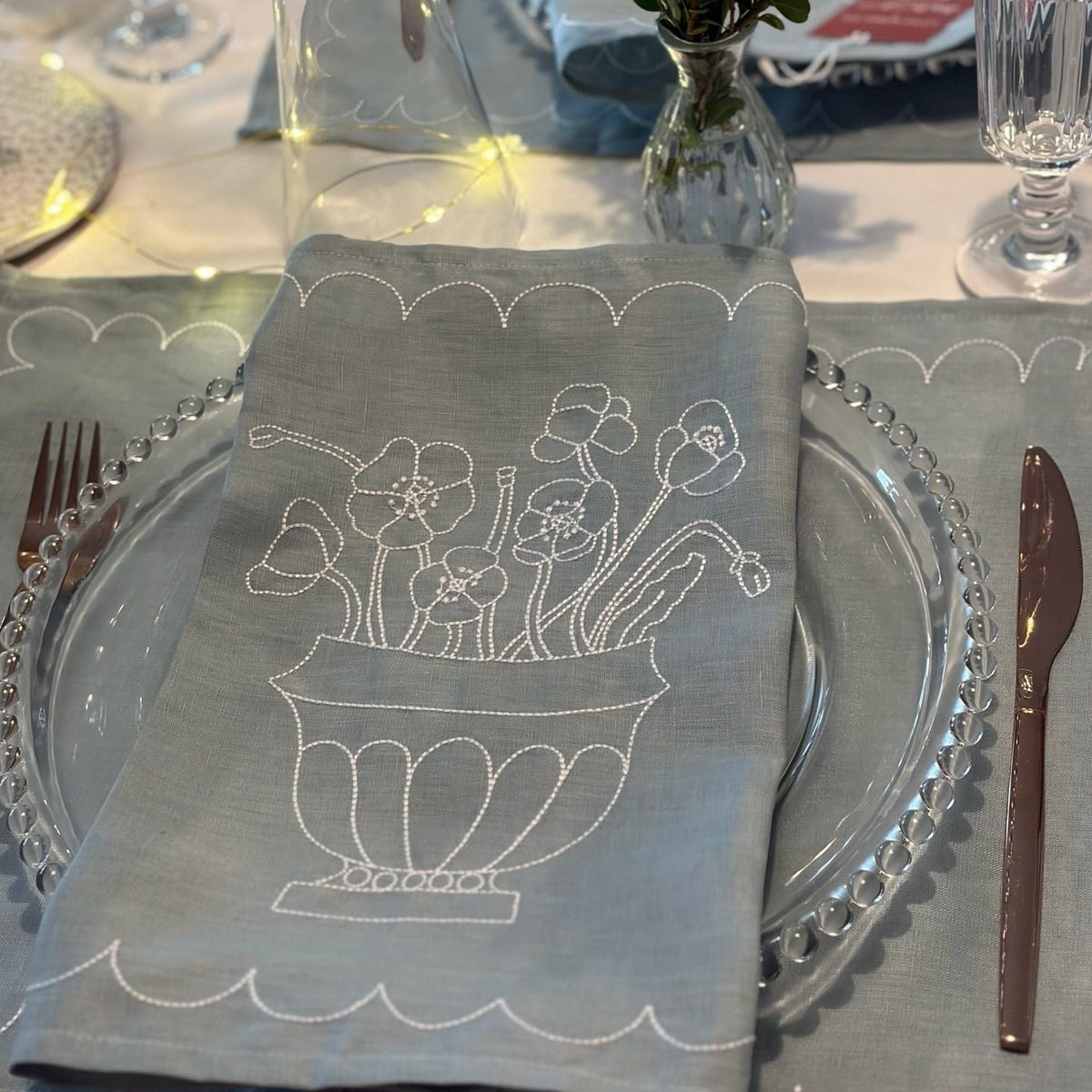 Decorative table setting with a blue napkin featuring floral embroidery on a white tablecloth.