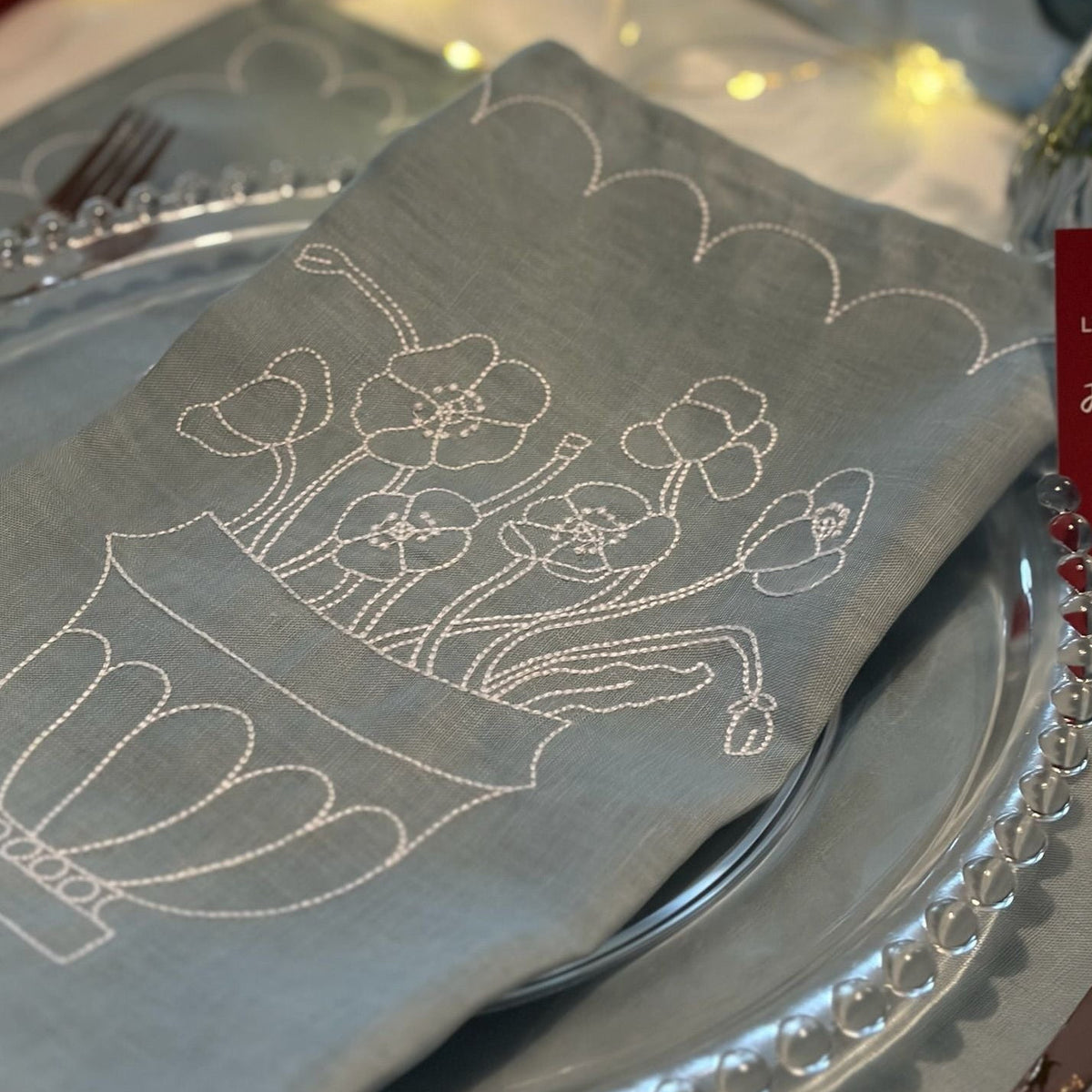 Napkin with floral embroidery on a table setting with silverware and plates.