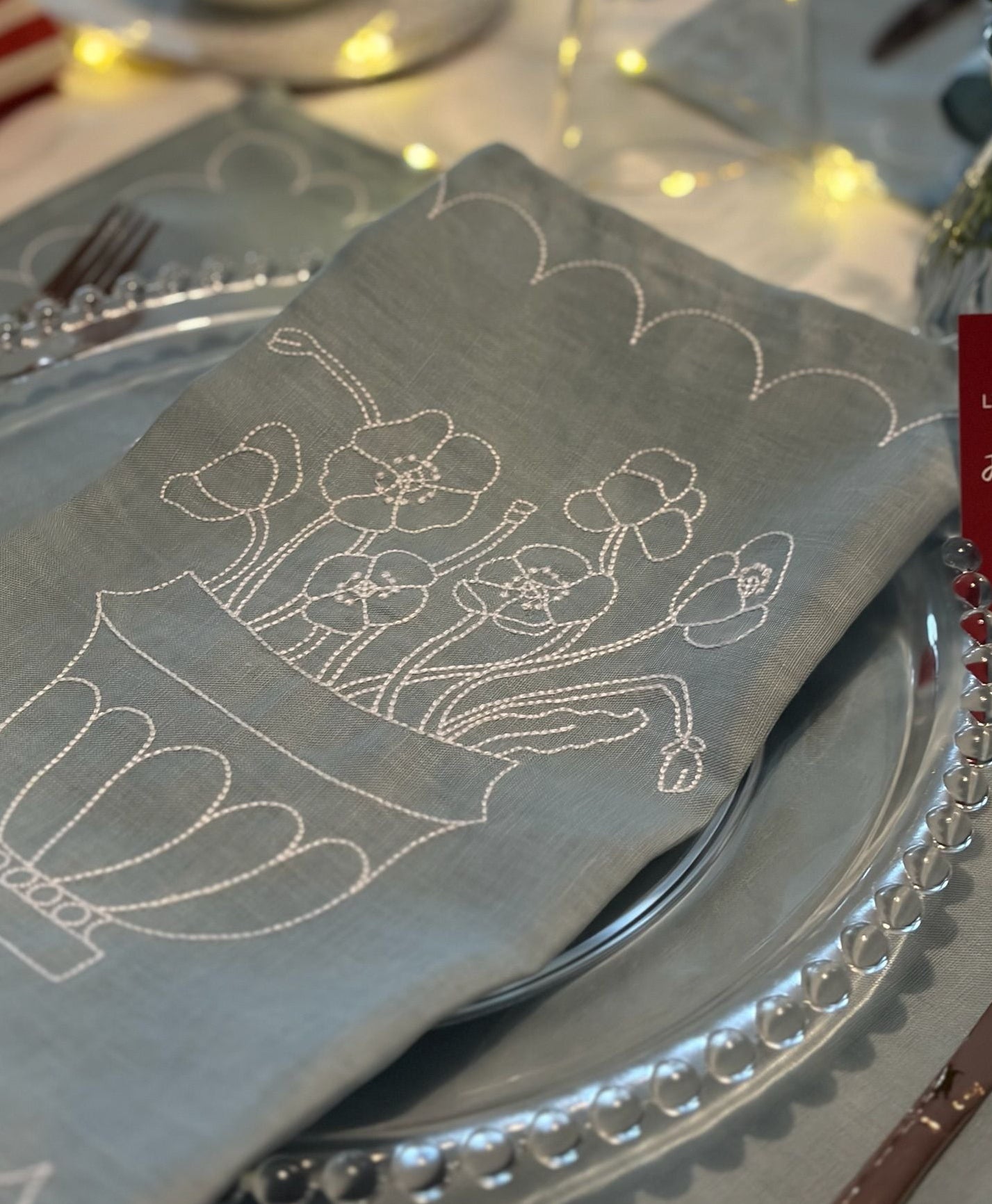 Napkin with floral embroidery on a table setting with silverware and plates.