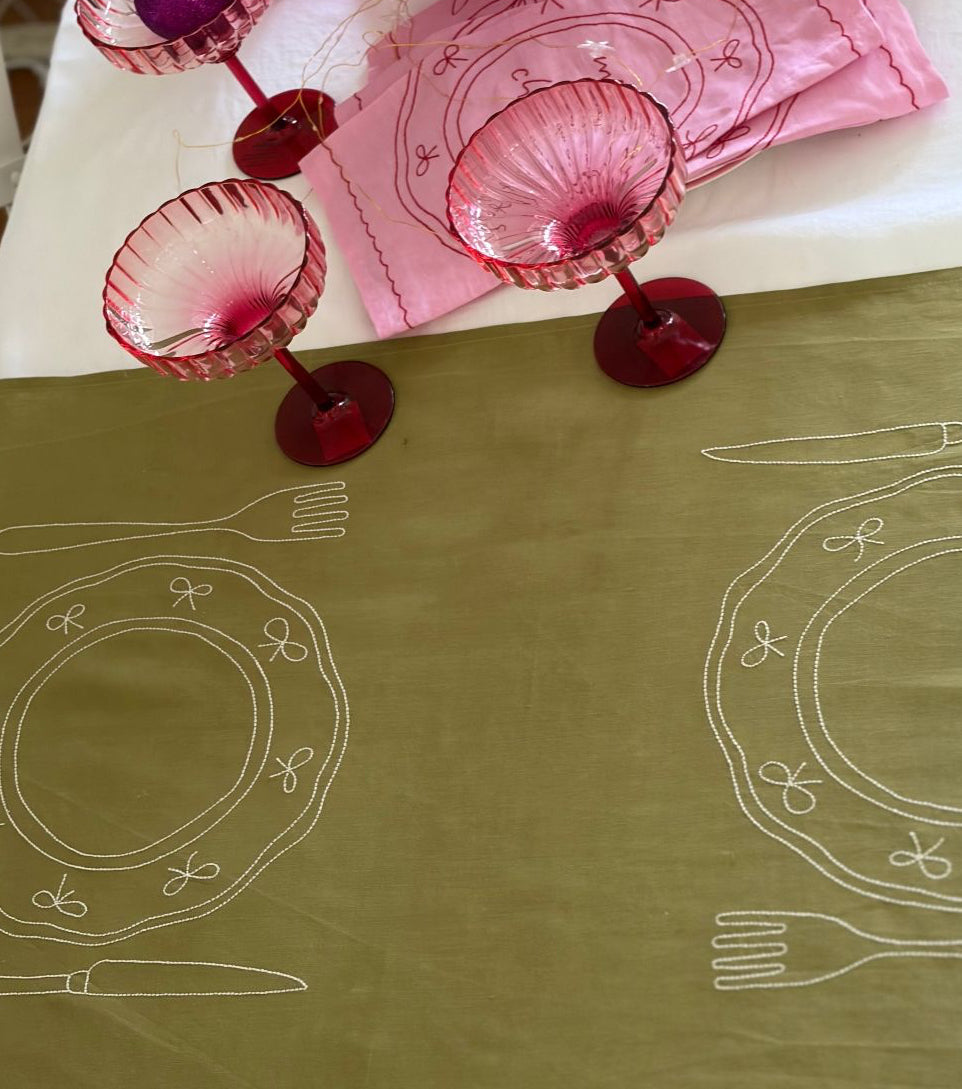 Green duo double placemat  with white line art and pink glassware on a white surface.