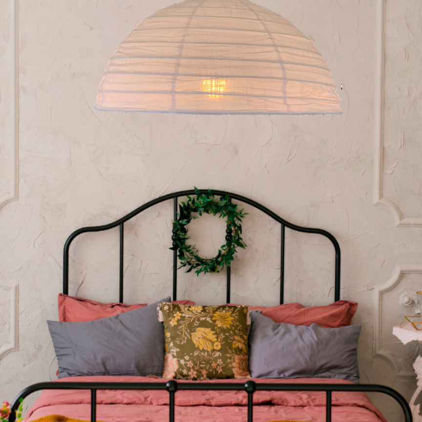 A blush pink linen light shade with a bamboo frame, hanging over a bed in an elegantly decorated bedroom, providing a warm glow to the space.
