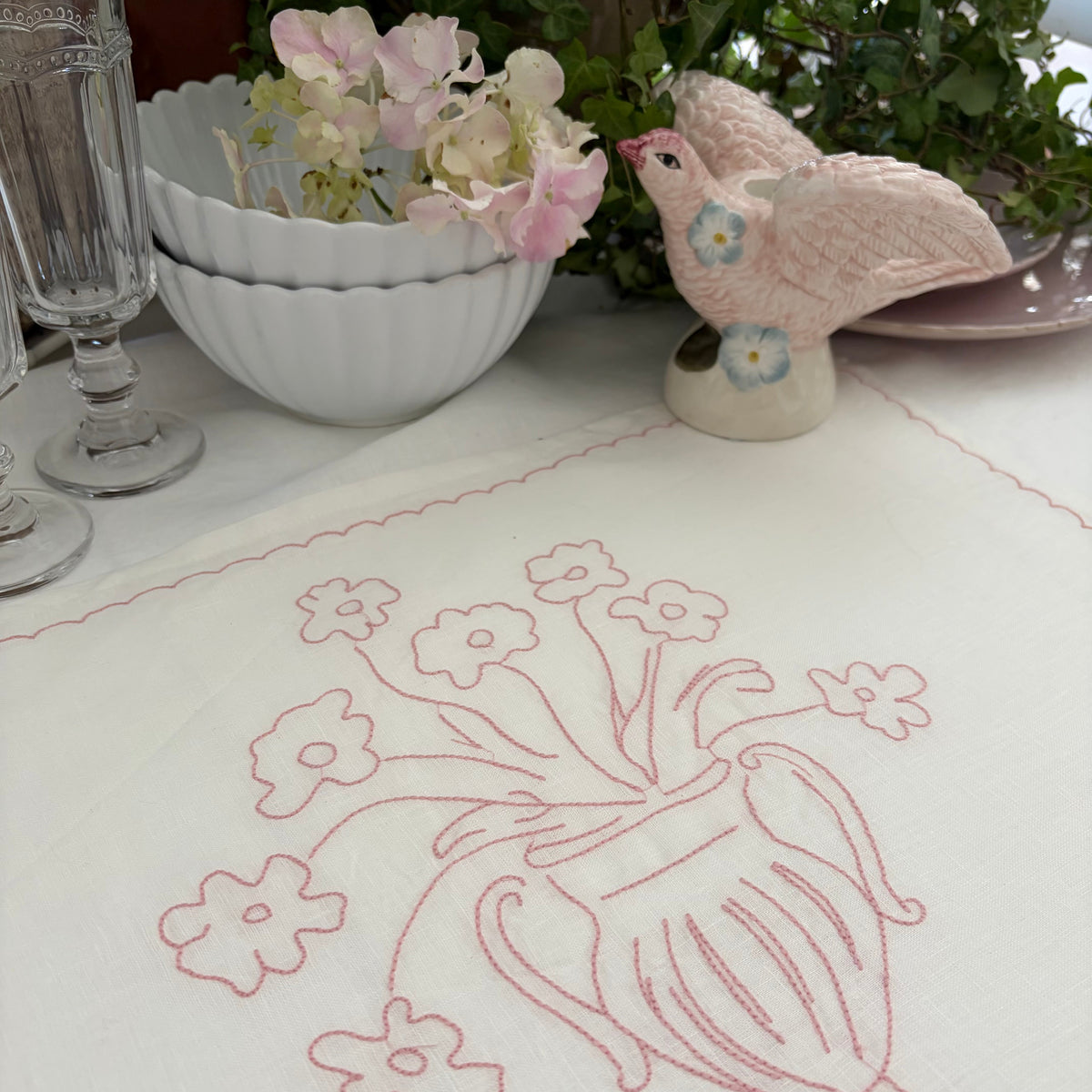 Little Nordic Sol Bloom pink embroidered linen placemat with floral urn design styled on a dining table.