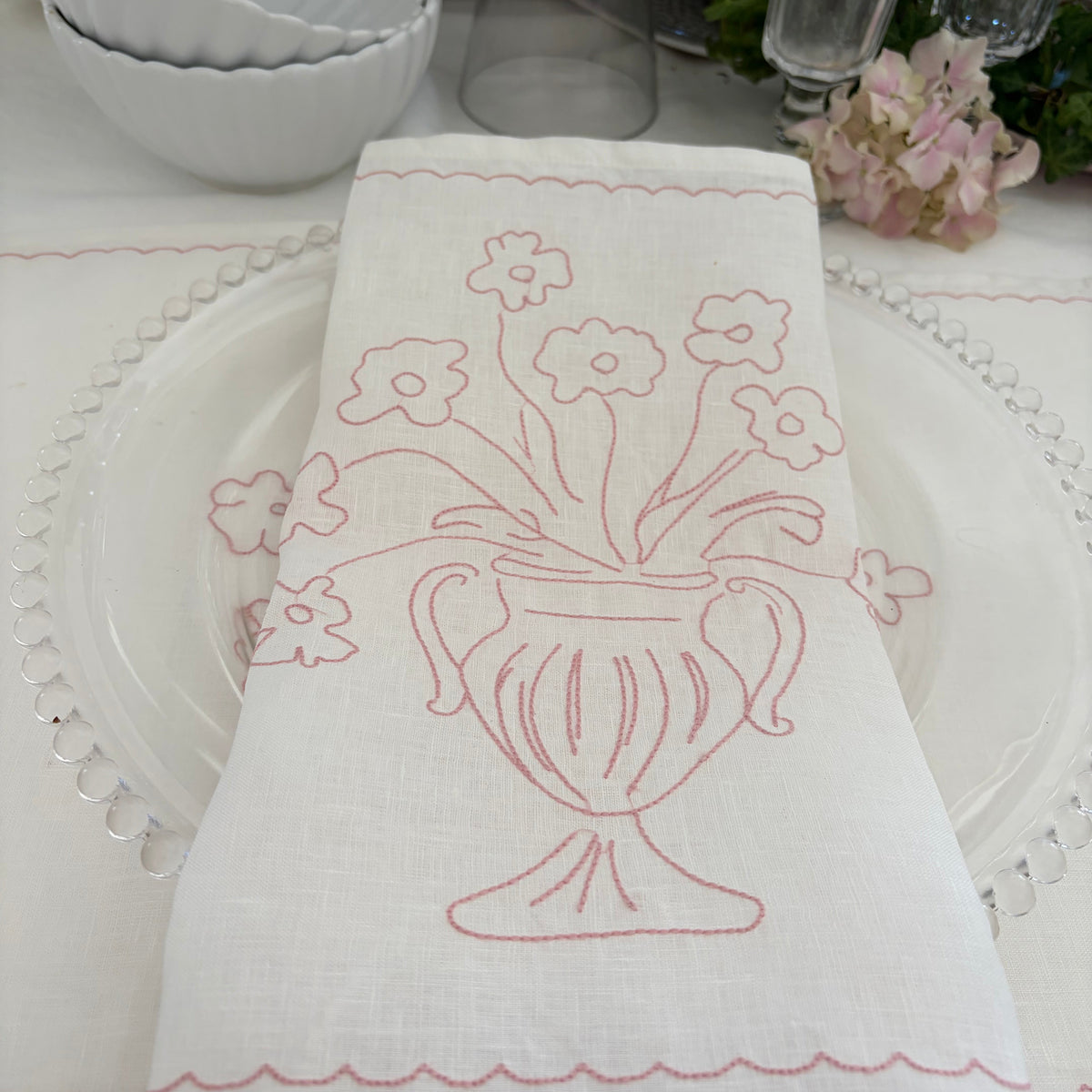 Little Nordic Sol Bloom pink embroidered linen placemat styled over a plate in a soft pink table setting.