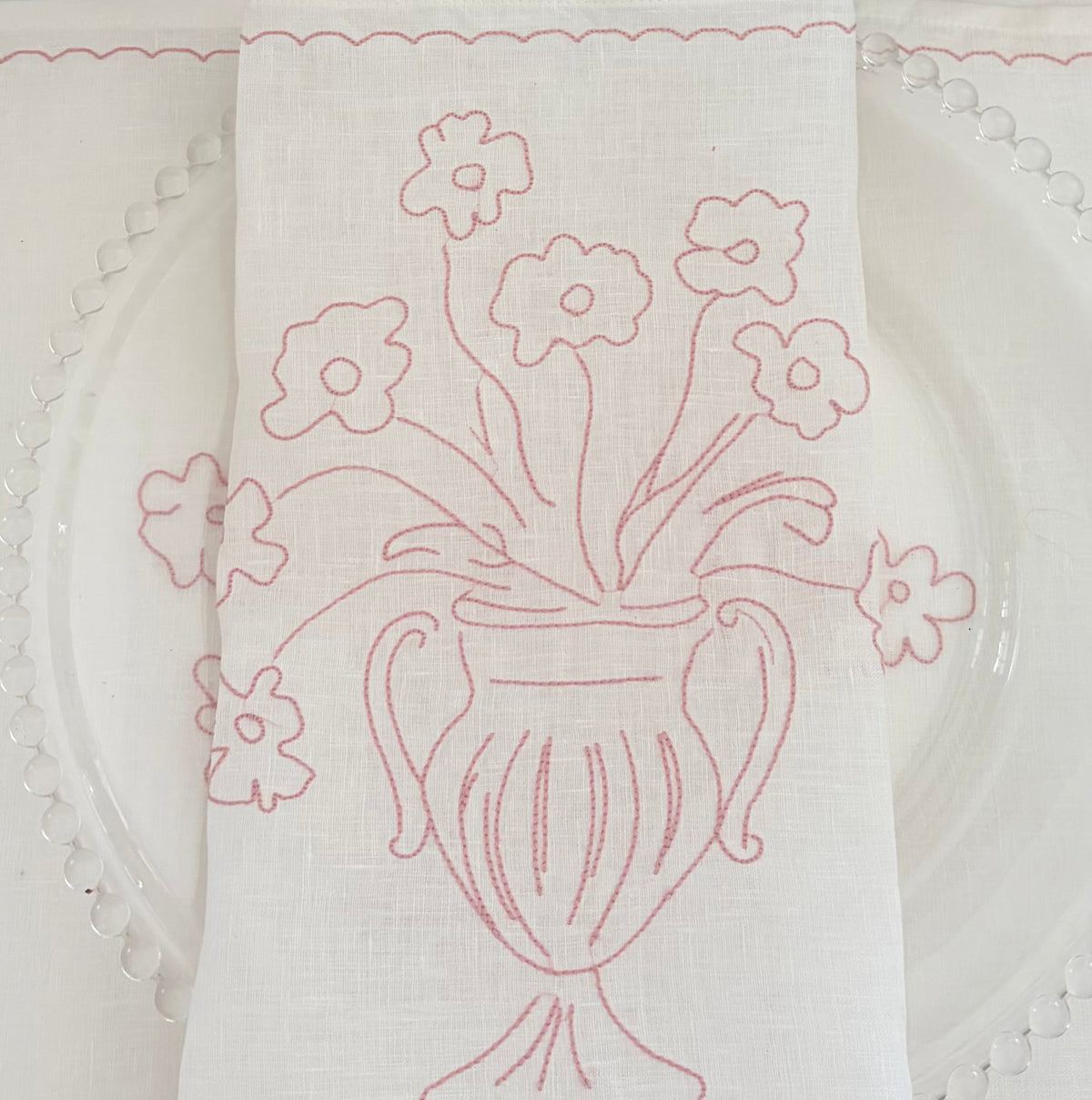 Little Nordic Sol Bloom pink embroidered linen placemat featuring a delicate floral vase motif on white linen.