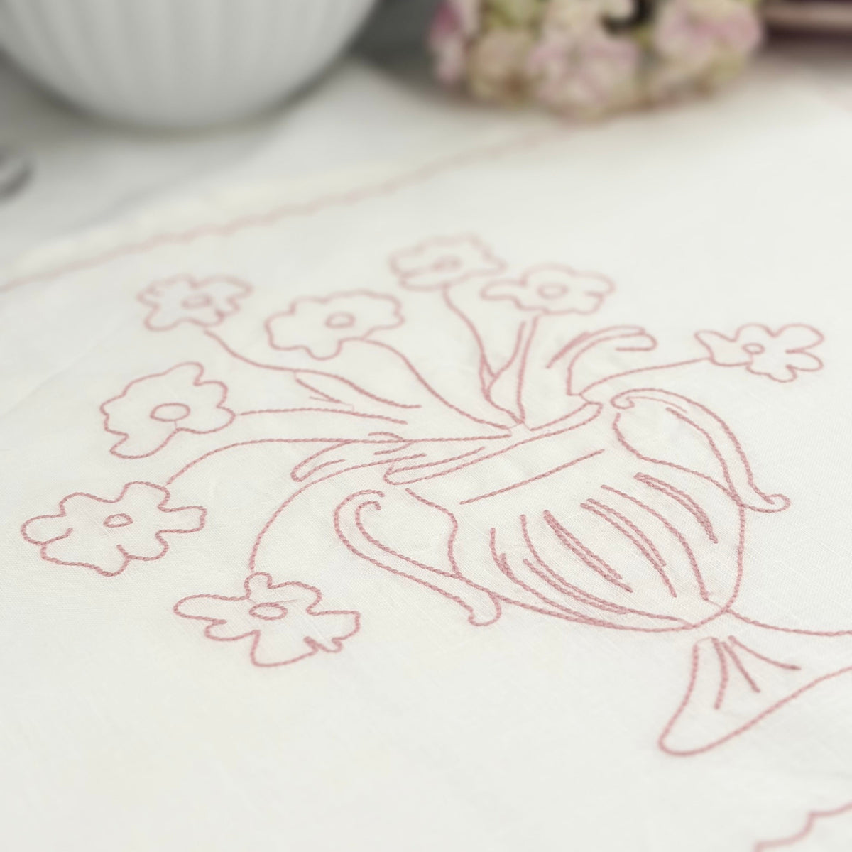 Close-up of Little Nordic Sol Bloom linen placemat showing pink floral urn embroidery on white linen.