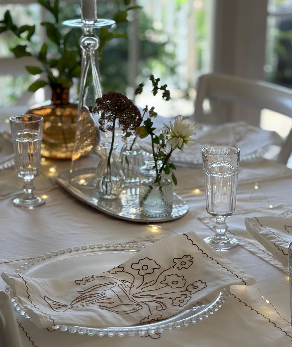 Elegant table setting with floral napkins, glasses, and a vase.