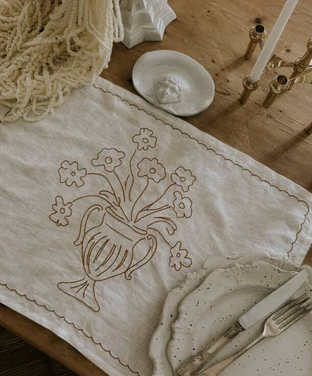 Embroidered table runner with floral and teapot design on a wooden table.