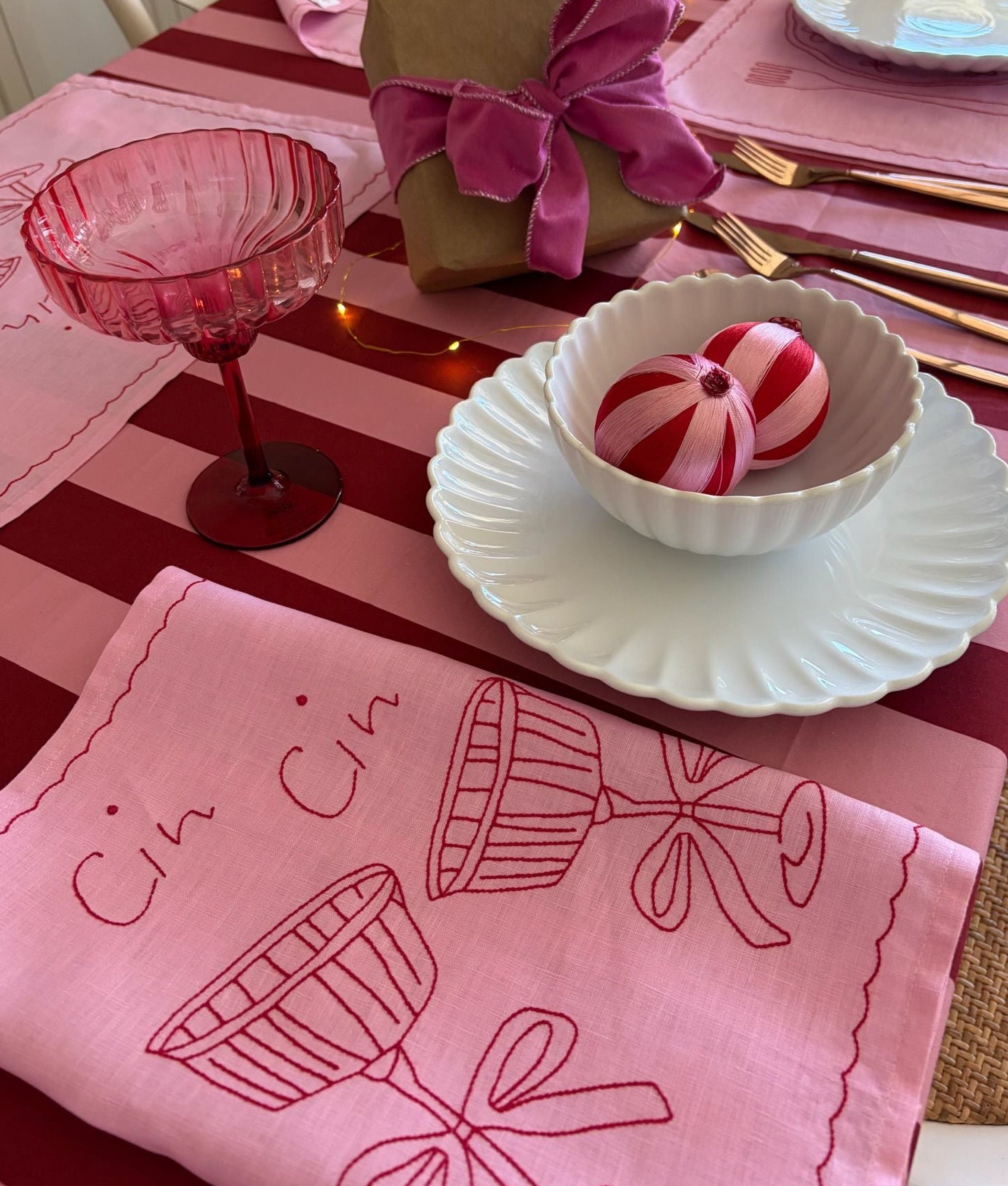 Pink table setting with a napkin featuring wine glass and bow designs, a bowl with a candy, and a glass.