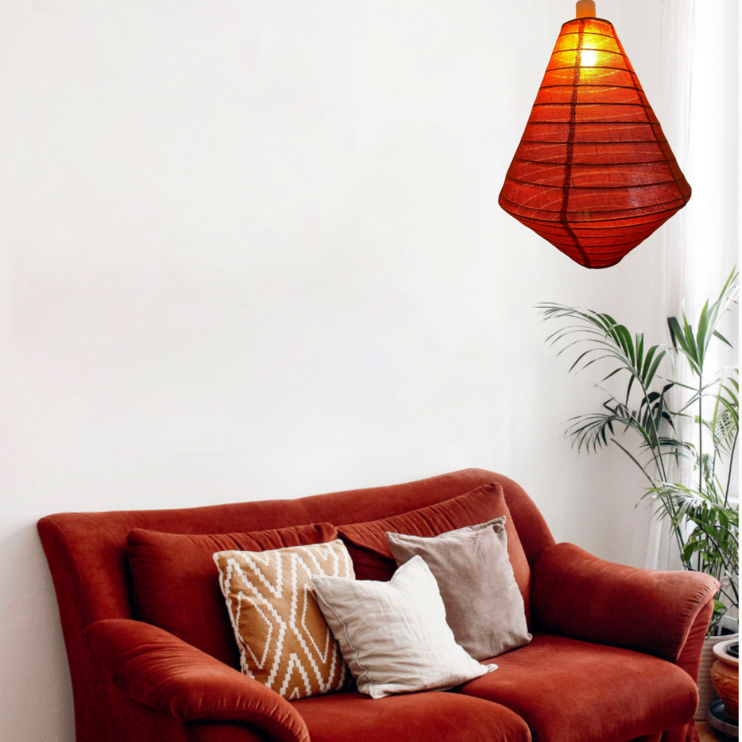 Red sofa with decorative pillows and a hanging rust linen lamp in a room with a plant.