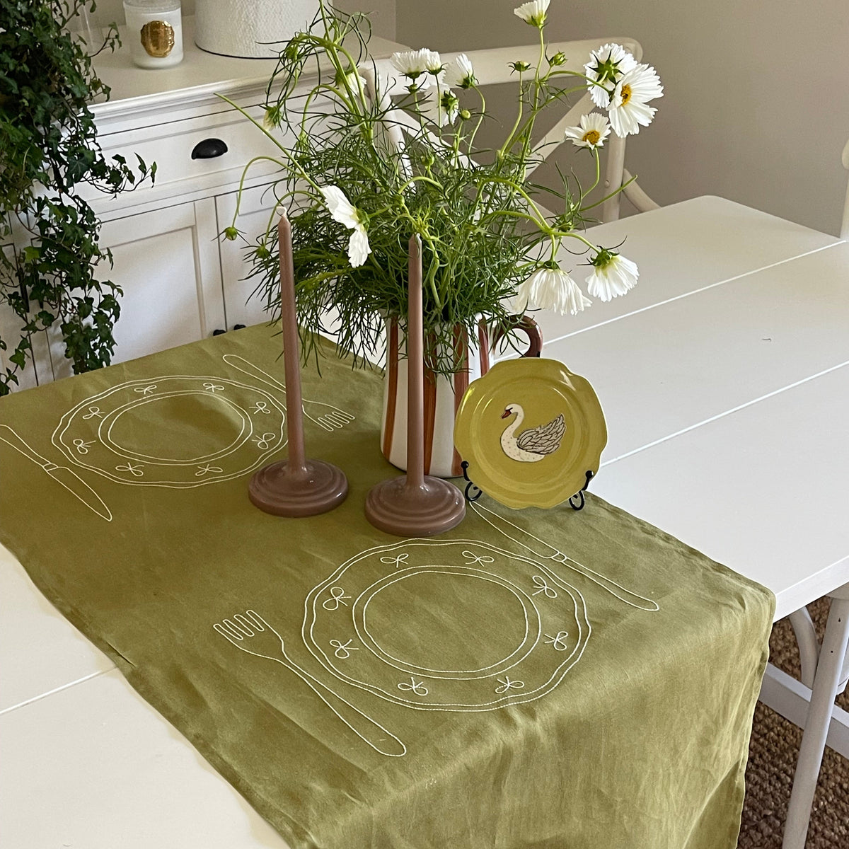 Little Nordic Sol Duo olive linen placemat with white embroidered plate design styled on a dining table.