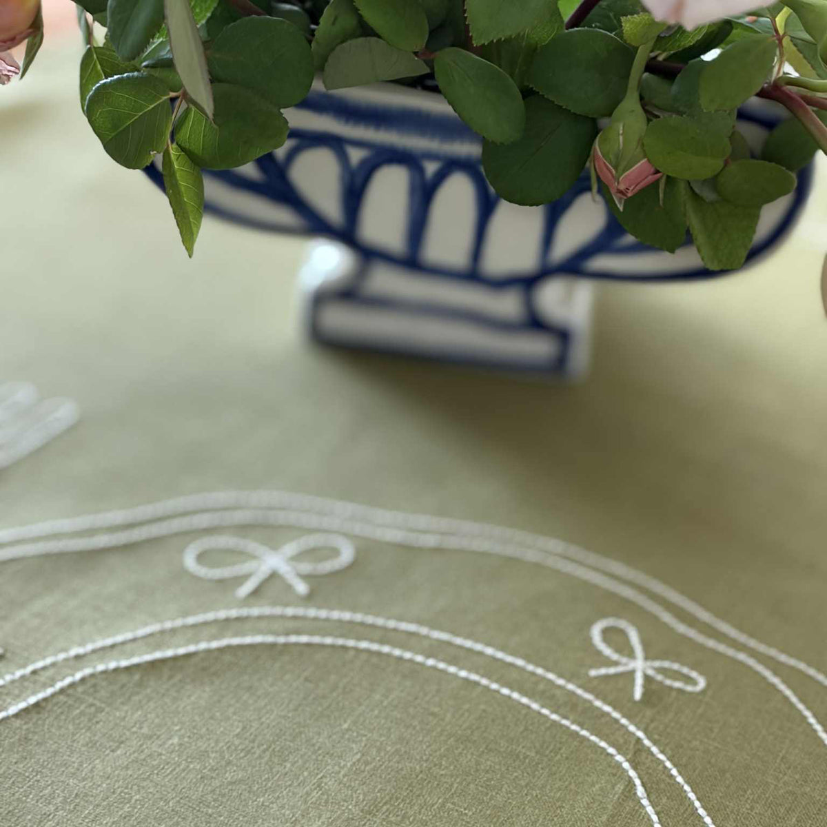 Close-up of Little Nordic Sol Duo olive linen placemat featuring white embroidered plates and cutlery and stitching