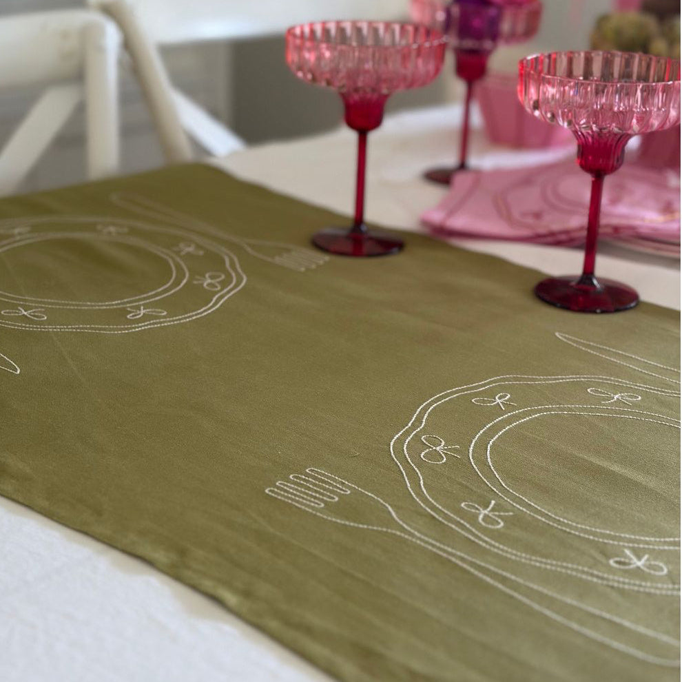 Little Nordic Sol Duo olive linen placemat with embroidered place settings styled with pink glassware.