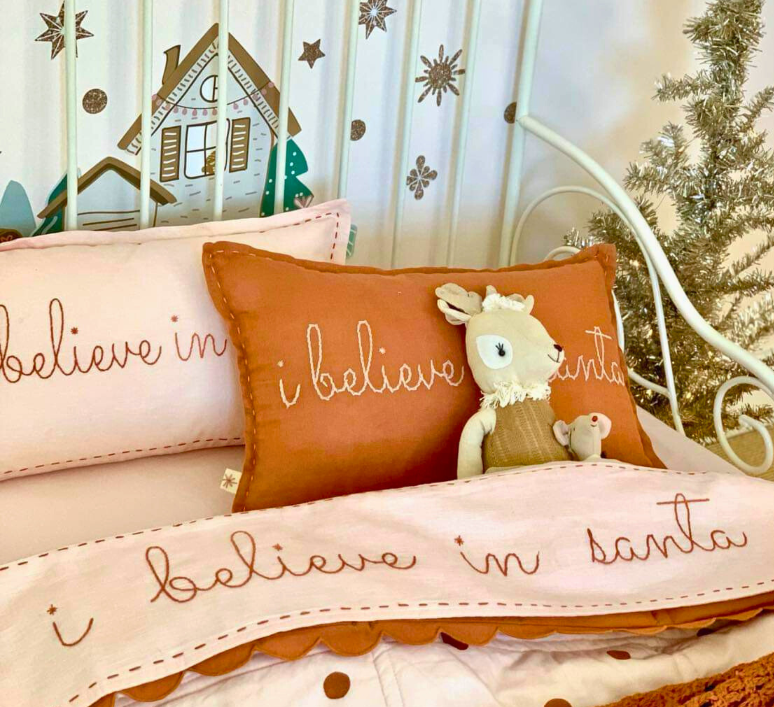 Decorative pillows with 'I believe in Santa' text and a plush toy on a bed with Christmas-themed bedding.