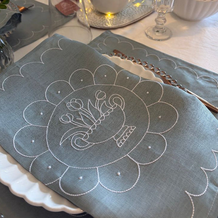 Embroidered blue placemat with floral design on a table setting.