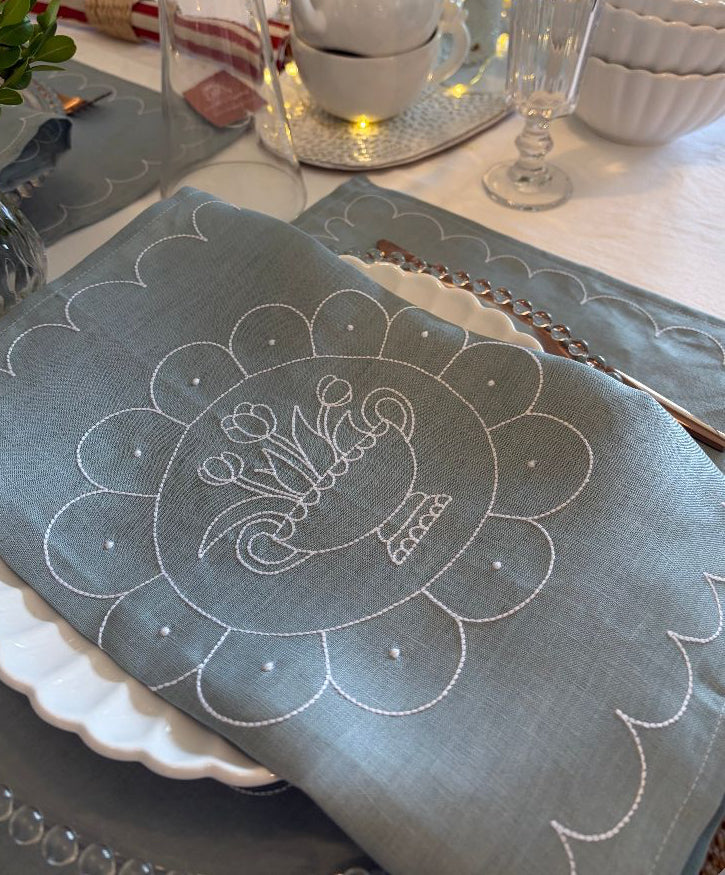 Embroidered blue placemat with floral design on a table setting.
