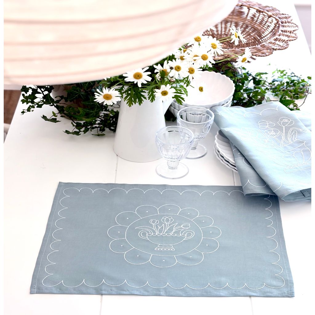 Light blue placemat with floral design on a table setting with flowers and glasses.