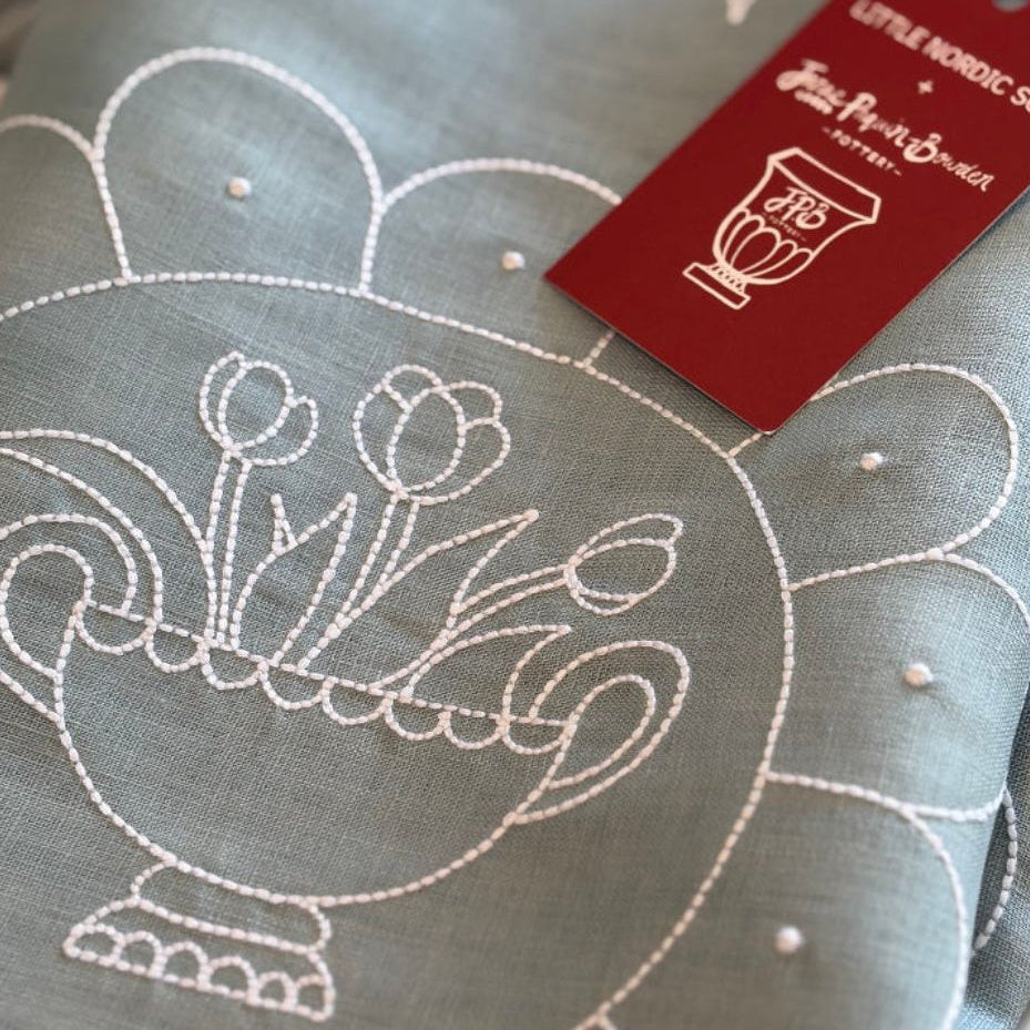 Embroidered fabric with floral design and brand tag on a blue background Janae Paquin-Bowden design