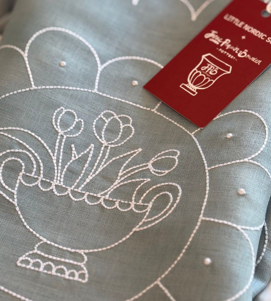 Embroidered fabric with floral design and brand tag on a blue background Janae Paquin-Bowden design