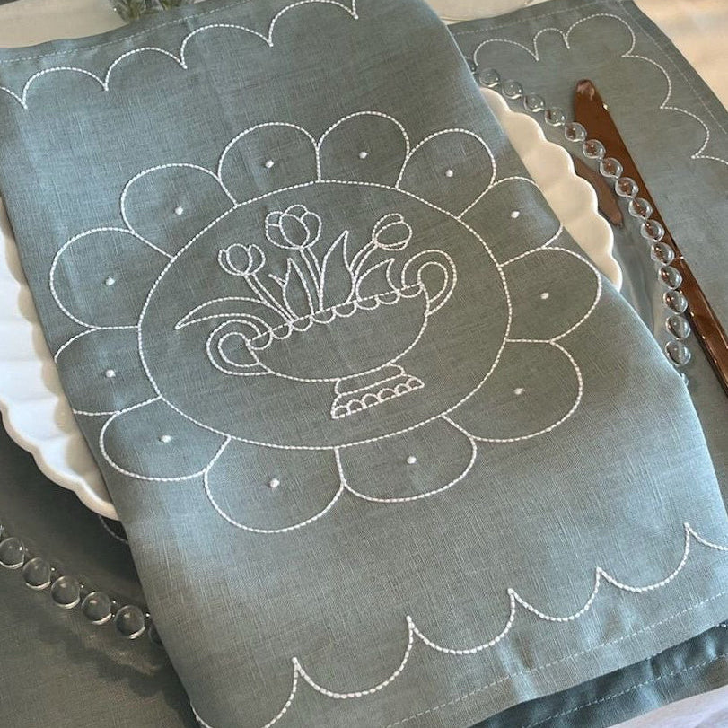 Dining table setting with blue placemats and embroidered napkins.