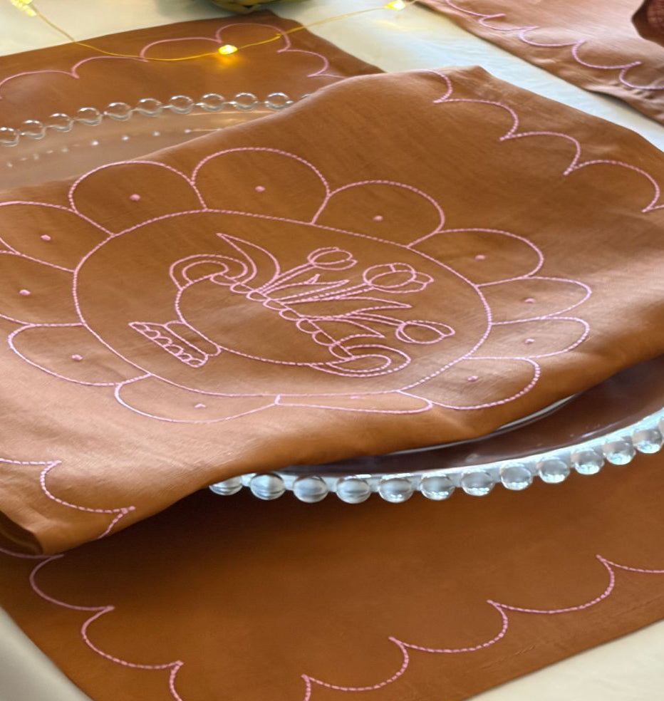 tan placemat with pink floral embroidery on  a plate