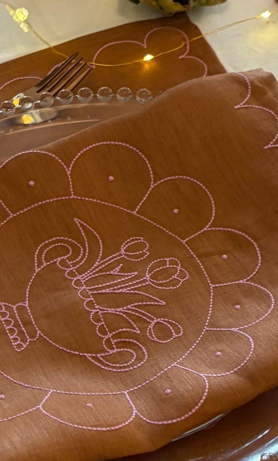 Brown placemat with white embroidery on a wooden table.